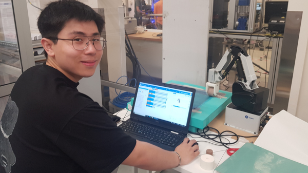 Luca Lu next to the DOBOT MG400 during his NextCOMP internship at UOB, 2022